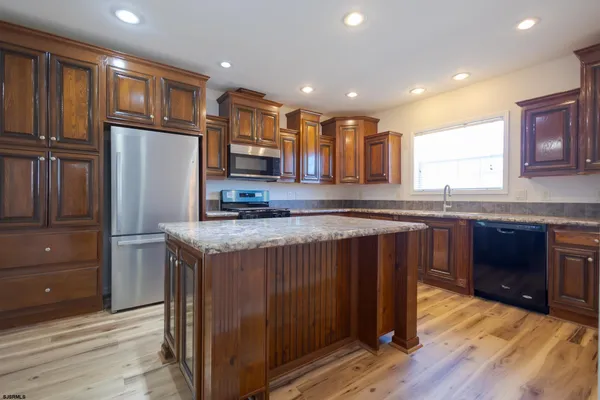 a kitchen with kitchen island granite countertop wooden cabinets a refrigerator a sink and dishwasher with wooden floor