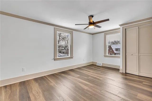 an empty room with wooden floor chandelier fan and windows
