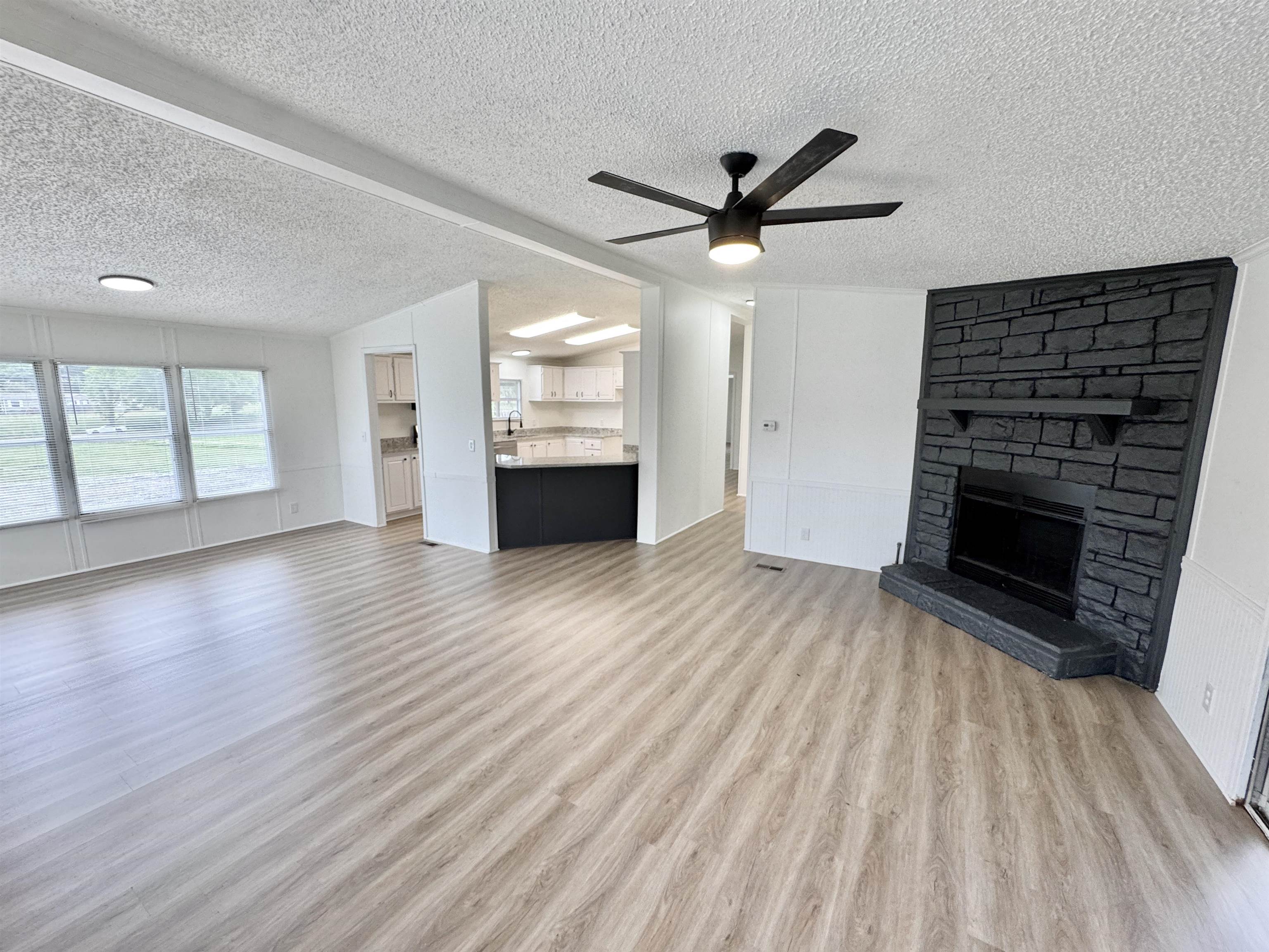 841 Simmons Road Drummonds, TN 38023 - Photo 7 of 35 Unfurnished living room featuring a textured ceiling, light wood-type flooring, ceiling fan, and a stone fireplace