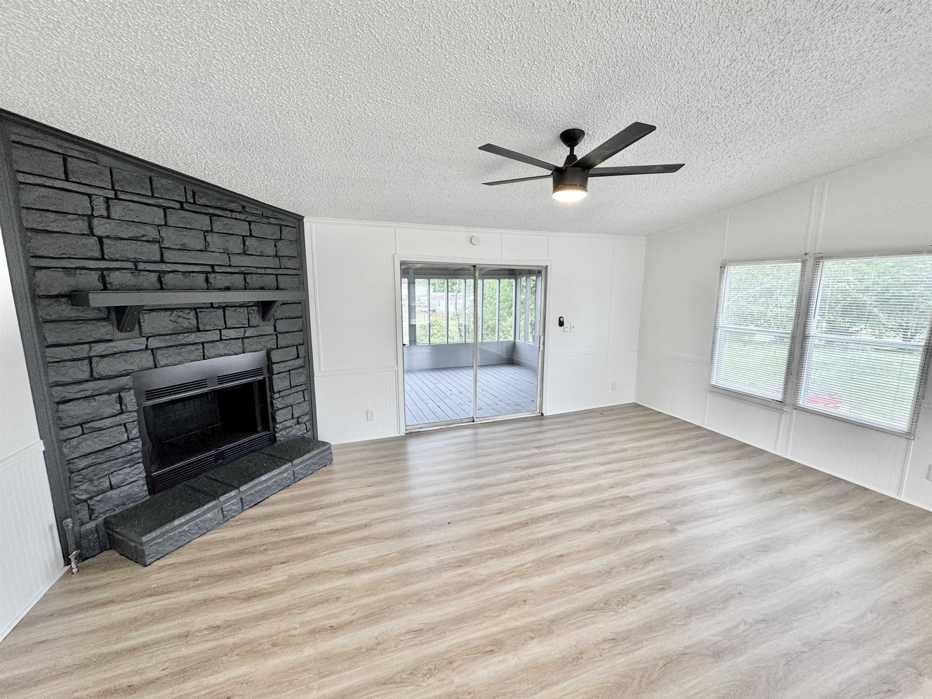 841 Simmons Road Drummonds, TN 38023 - Photo 8 of 35 Unfurnished living room with vaulted ceiling, a textured ceiling, wood finished floors, a ceiling fan, and a stone fireplace