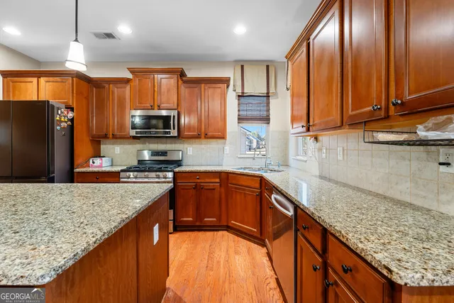 a open kitchen with stainless steel appliances granite countertop wooden floors wooden cabinets a stove a sink and a center island