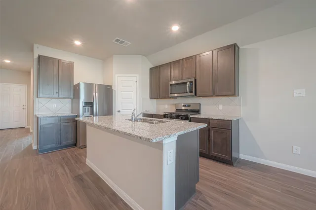 a kitchen with stainless steel appliances granite countertop a stove a sink dishwasher a refrigerator and a oven with wooden floor