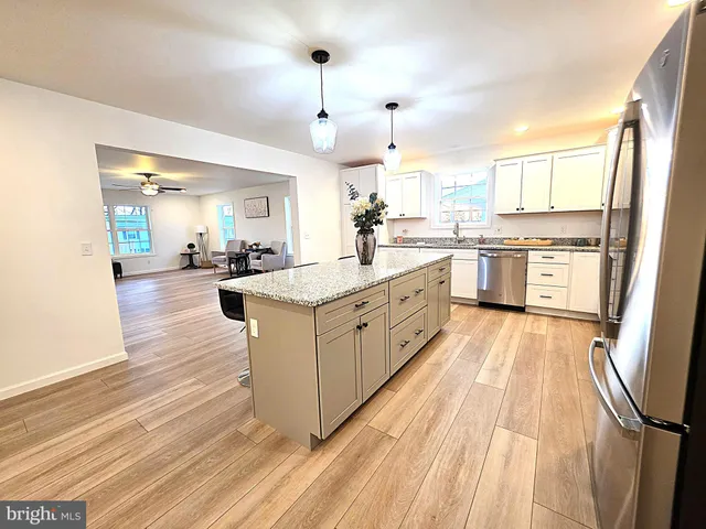 a large kitchen with kitchen island a sink dishwasher stove and white cabinets with wooden floor