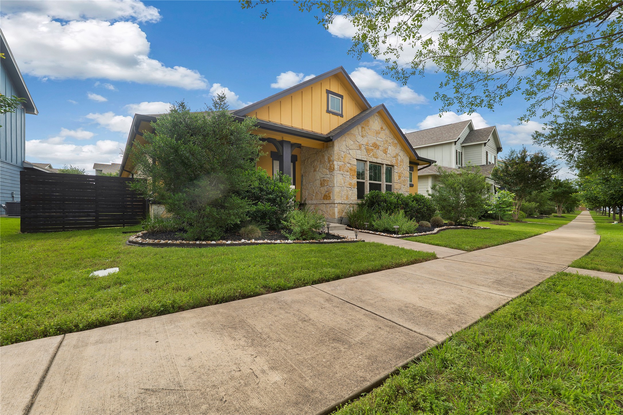 8721 Sikes Way Austin, TX 78747 - Photo 27 of 33 Stone and siding exterior featuring a covered entry, established landscaping, a black horizontal slat fence, and a sidewalk border