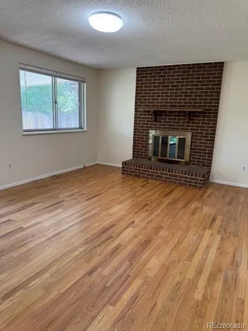 a view of an empty room with wooden floor fireplace and a window