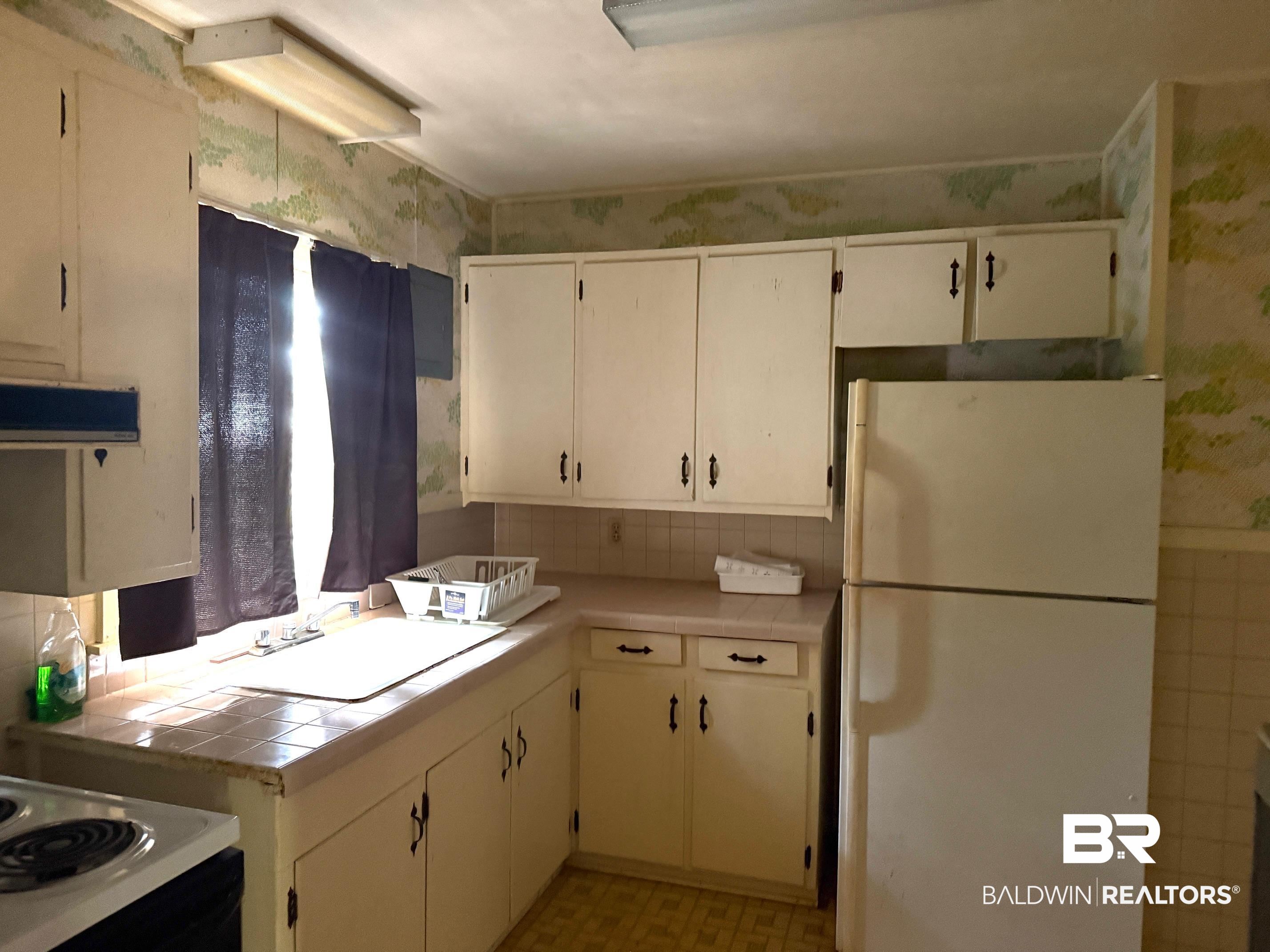 156 Pier Avenue Fairhope, AL 36532 - Photo 22 of 41 Kitchen featuring white appliances, wallpapered walls, tile counters, light flooring, and white cabinetry