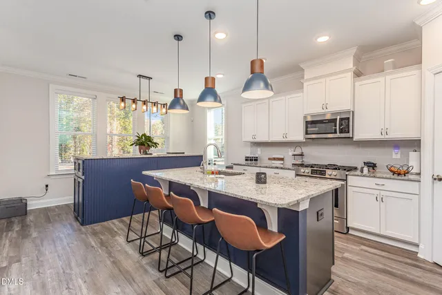 a kitchen with stainless steel appliances granite countertop a stove a refrigerator a kitchen island a sink dishwasher and a dining table with wooden floor