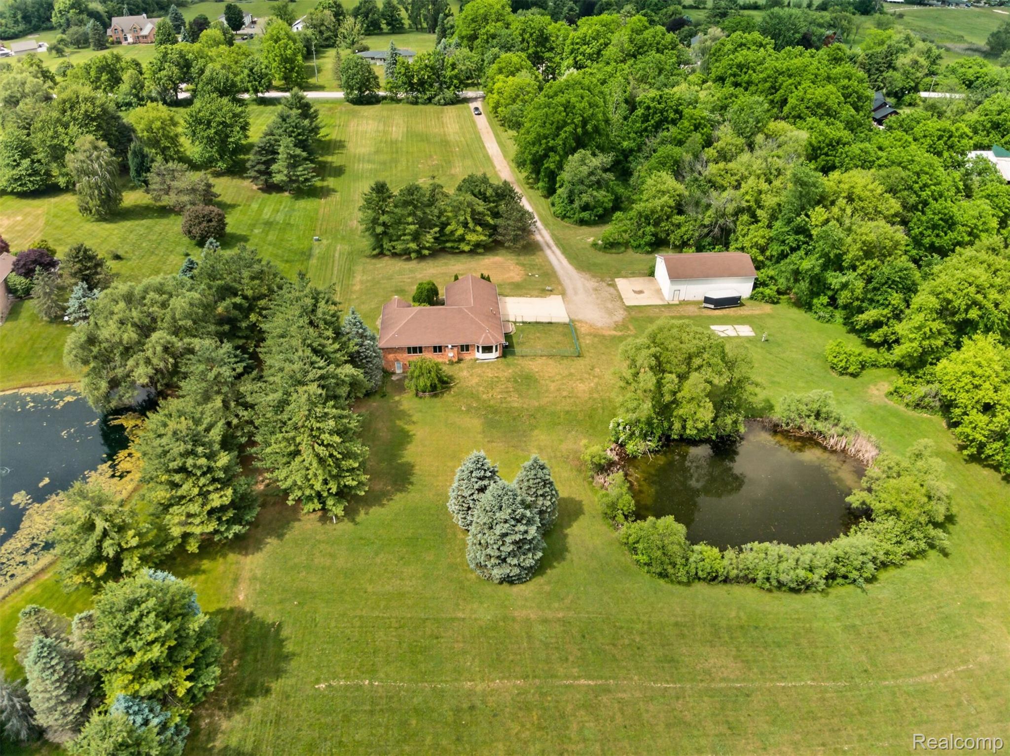 8558 37 Mile Road Romeo, MI 48065 - Photo 2 of 29 Expansive property featuring a brick residence with a brown roof, two distinct ponds, a white outbuilding, and mature trees encompassing the perimeter