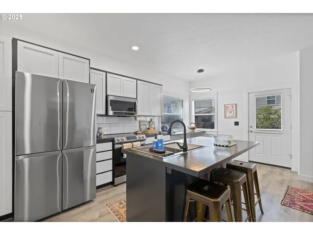 a kitchen with stainless steel appliances granite countertop a refrigerator a sink a stove a dining table and chairs