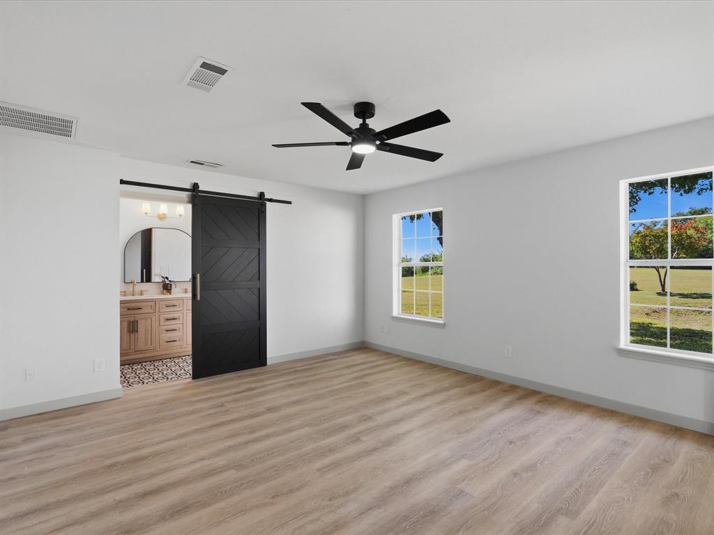 289 County Road 4655 Rhome, TX 76078 - Photo 10 of 34 Spacious interior featuring wood-finish flooring, a modern black ceiling fan, and two large windows providing natural light