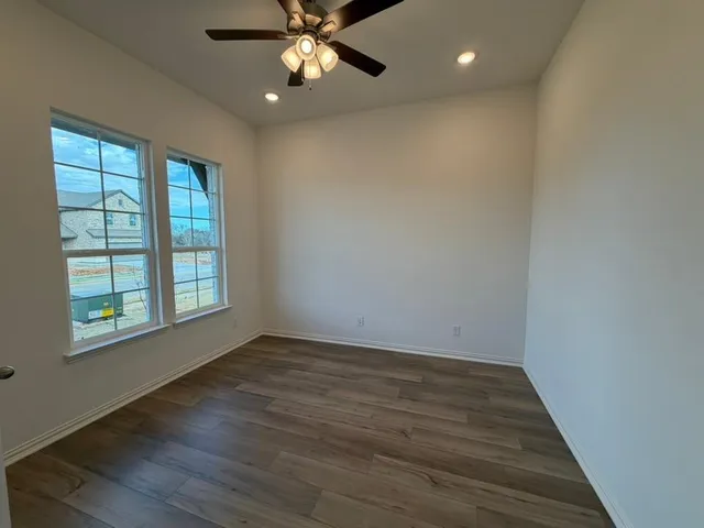 an empty room with wooden floor chandelier fan and windows