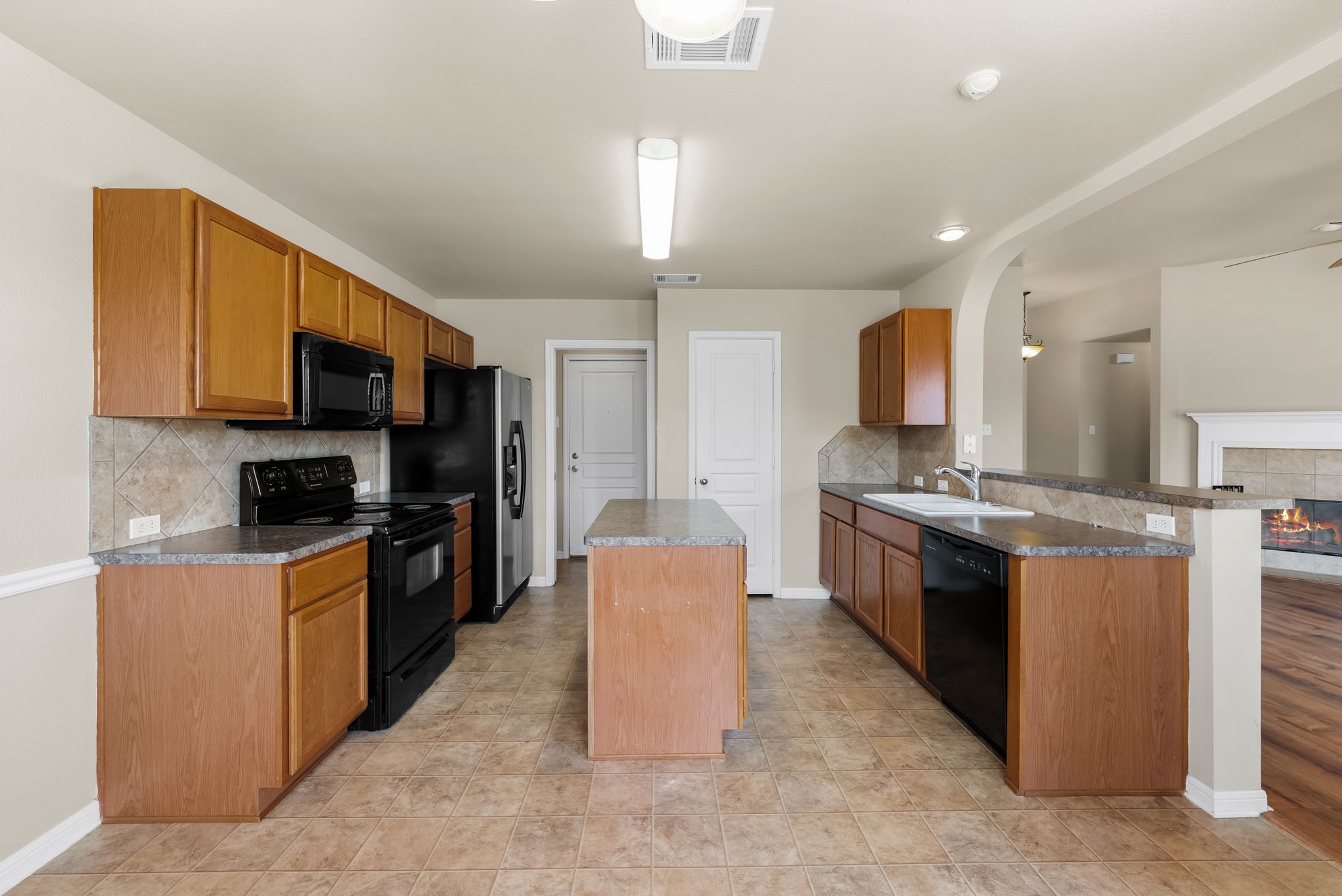 7719 Fieldstone Drive Temple, TX 76502 - Photo 18 of 37 Kitchen with backsplash, black appliances, wood finish cabinetry, a tile fireplace, and a peninsula