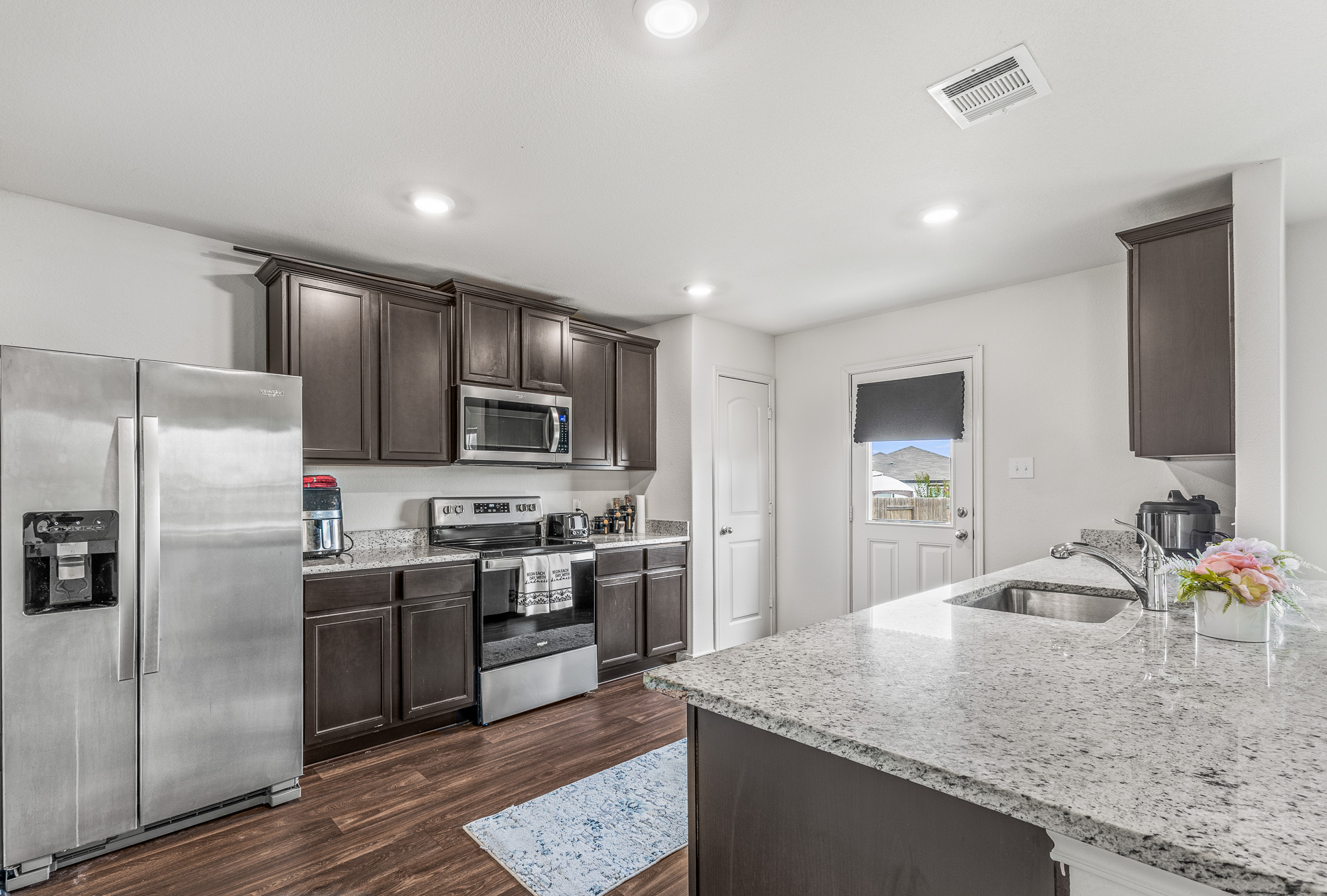 304 Hyacinth Way, Unit #7K Jarrell, TX 76537 - Photo 7 of 26 Brightly lit kitchen showcases dark wood cabinetry, granite counters, and modern stainless steel appliances.