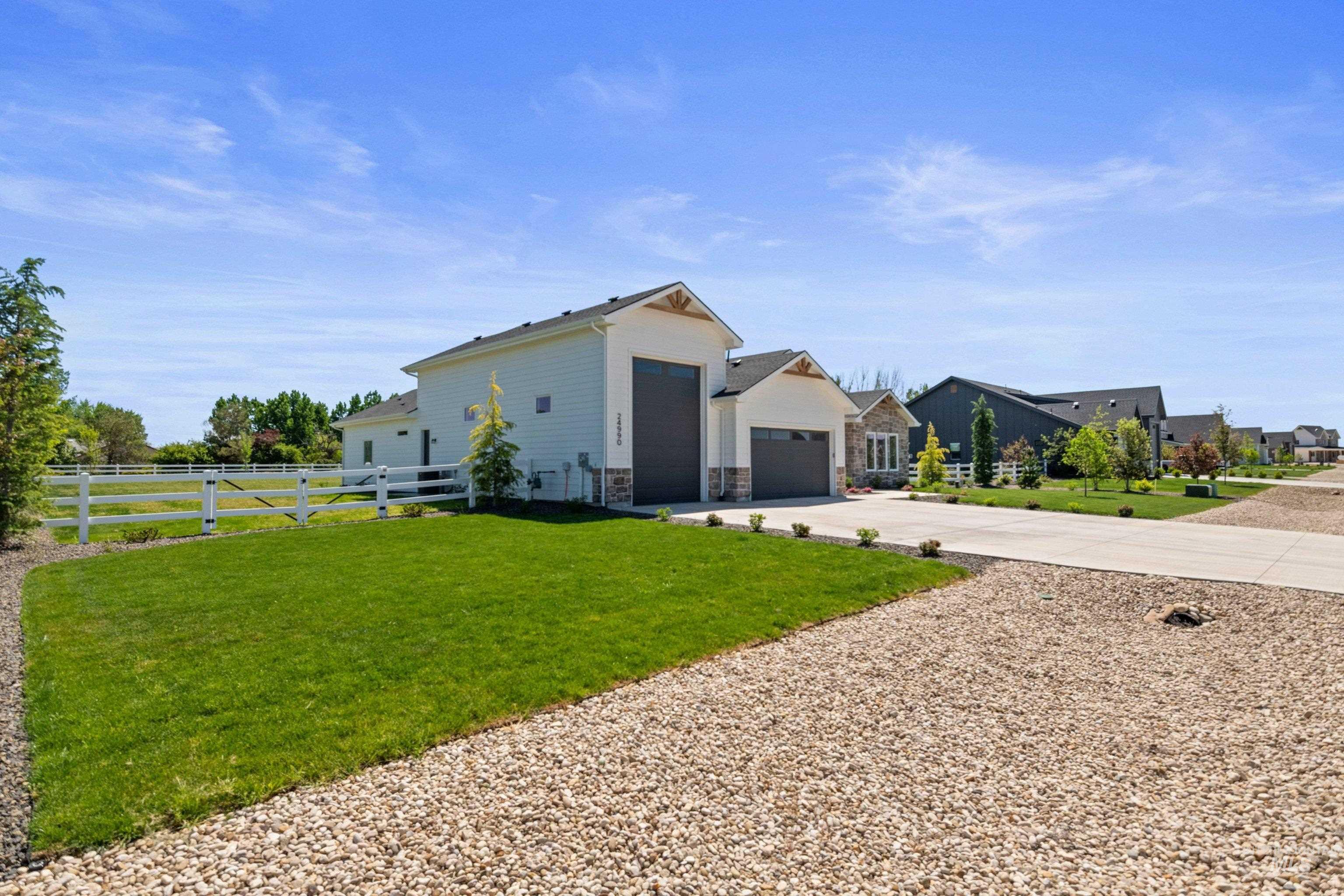 24990 Belgian Way Middleton, ID 83644 - Photo 4 of 50 Contemporary residence featuring a white siding exterior with stone accents, a multi-car garage, and a wide concrete driveway