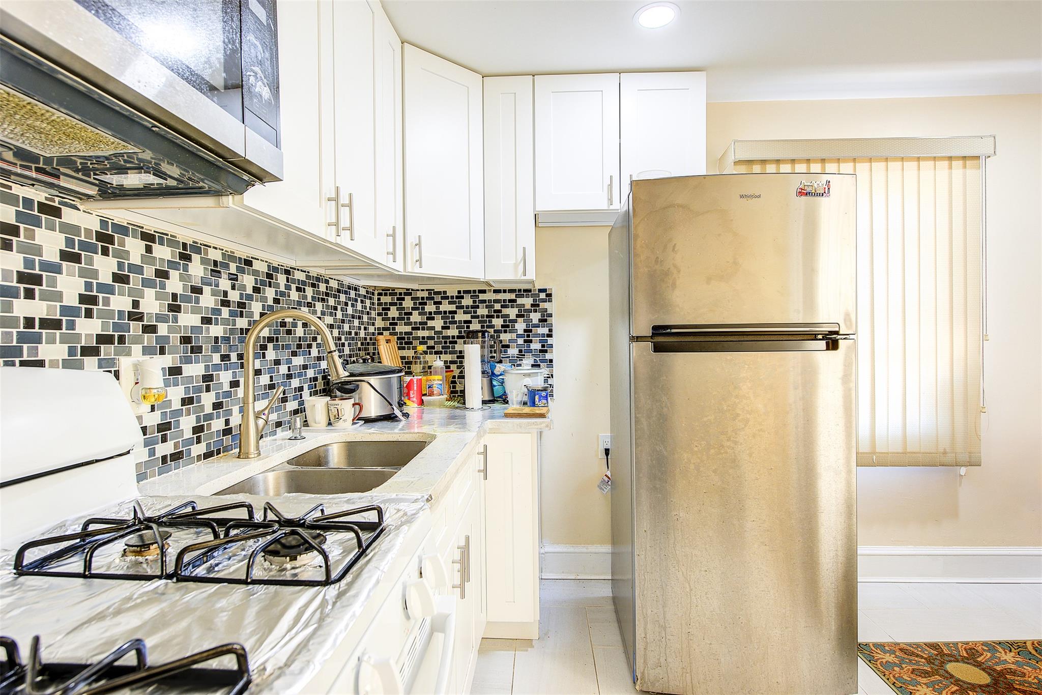 89-91 215th Place Queens, NY 11427 - Photo 12 of 16 Kitchen featuring white cabinets, light stone countertops, tasteful backsplash, and stainless steel appliances