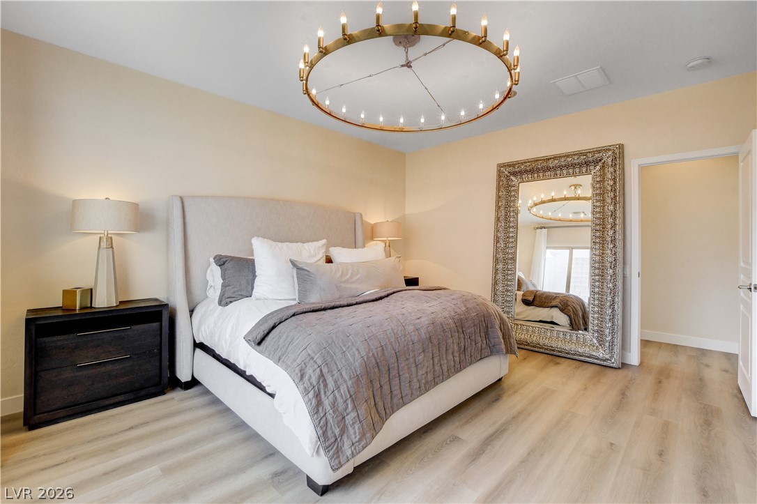 2649 Rue Marquette Avenue Henderson, NV 89044 - Photo 55 of 55 Elegant primary bedroom offers light wood-look flooring and a distinctive ceiling chandelier.
