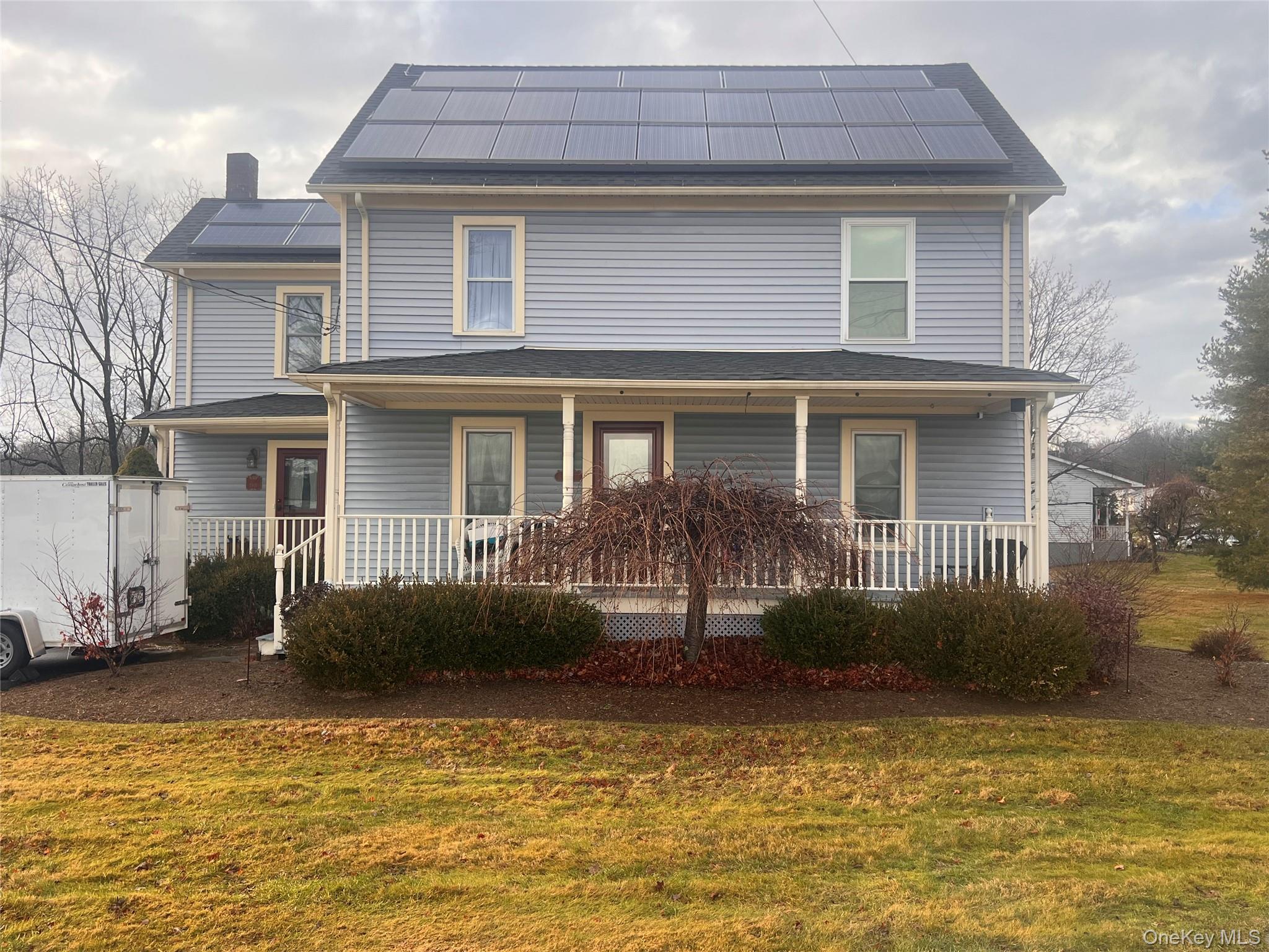View of front of house featuring solar panels, a porch, a front yard, and a chimney