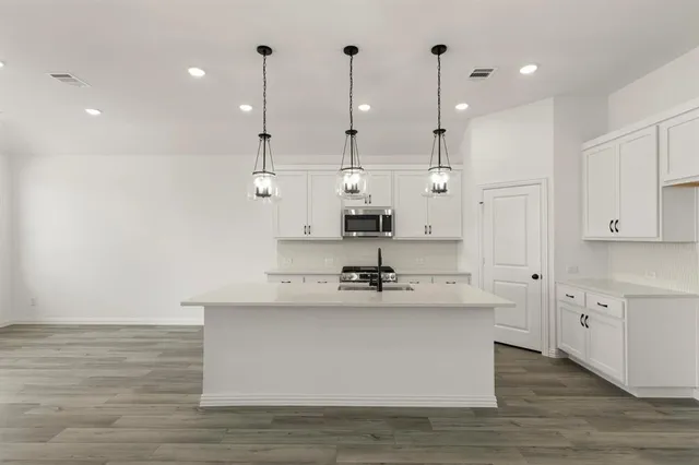 a large white kitchen with kitchen island a sink dishwasher a refrigerator and white cabinets with wooden floor