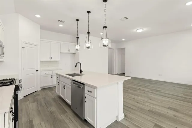 a kitchen with a sink a stove a refrigerator and white cabinets with wooden floor