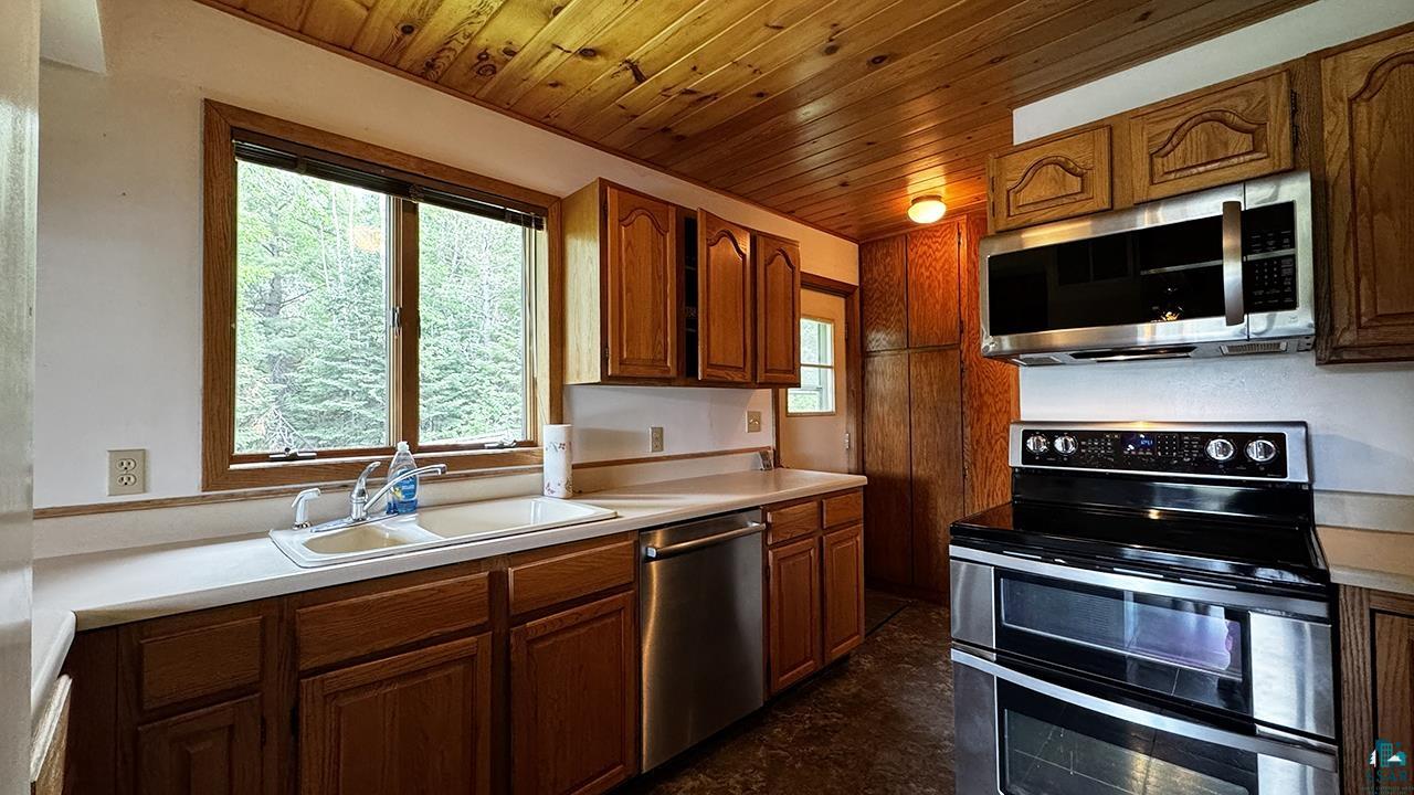 9289 Heino Road Angora, MN 55703 - Photo 7 of 37 Kitchen featuring a wood-panel ceiling, wood cabinetry, stainless steel appliances, a double basin sink, and a window above the sink