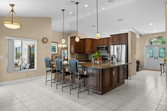 a kitchen with stainless steel appliances granite countertop a refrigerator a oven a sink a dining table and chairs with wooden floor