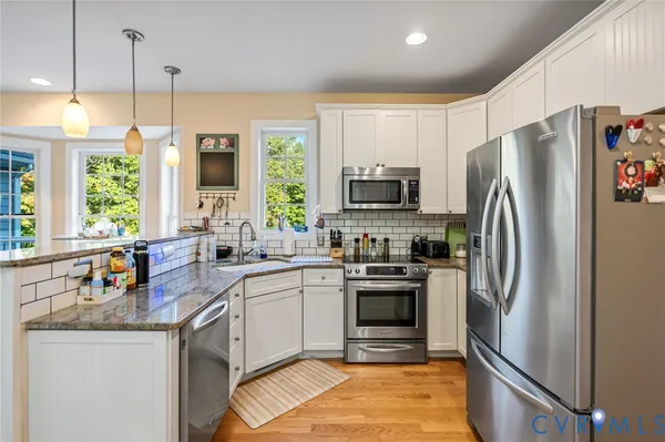 a kitchen with stainless steel appliances white cabinets a sink a stove a refrigerator and a center island