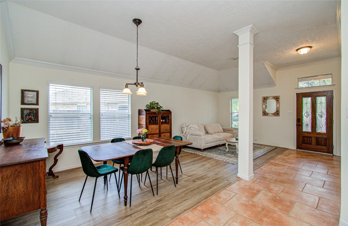 20007 Alcea Court Spring, TX 77379 - Photo 11 of 43 This inviting space features an open layout with a dining area and cozy living room. It has a mix of wood and tile flooring, a vaulted ceiling, and ample natural light from large windows. The entryway is welcoming with a stylish wooden door.
