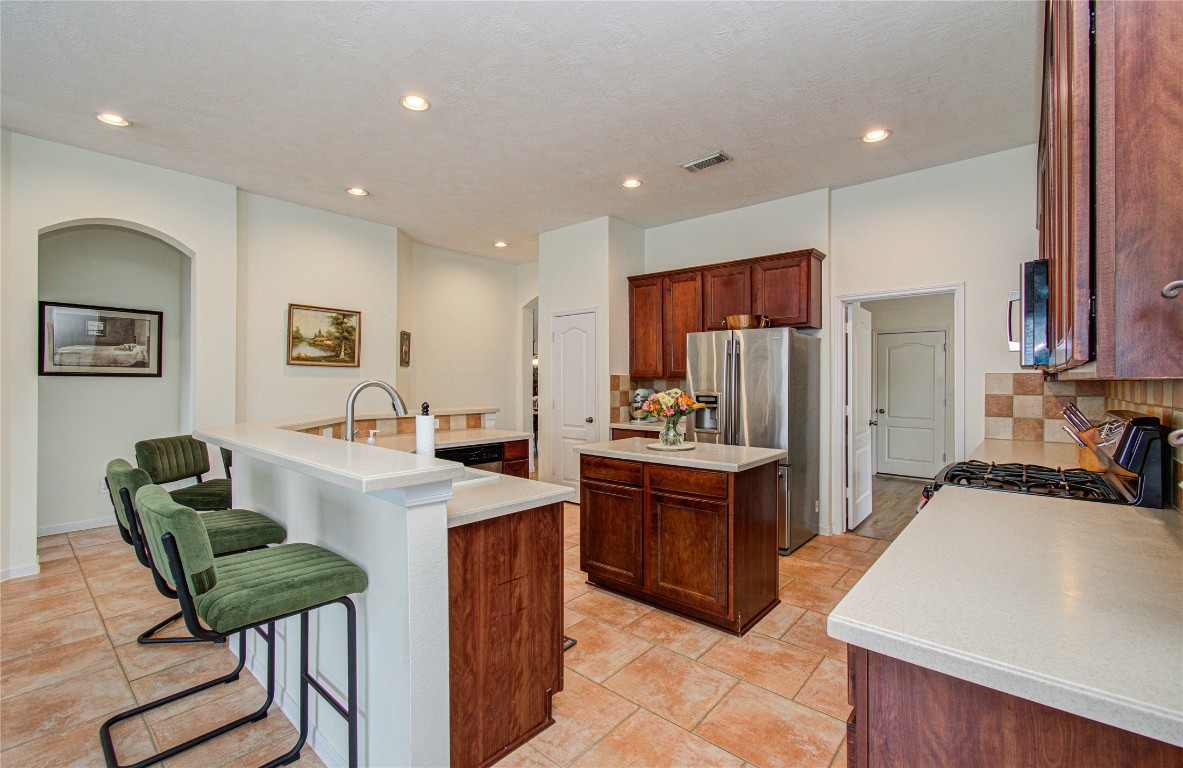 20007 Alcea Court Spring, TX 77379 - Photo 20 of 43 This kitchen features a spacious layout with a large island and bar seating. It has stainless steel appliances, warm wood cabinetry, and tiled flooring. The space is well-lit with recessed lighting and has neutral walls, creating an inviting atmosphere.