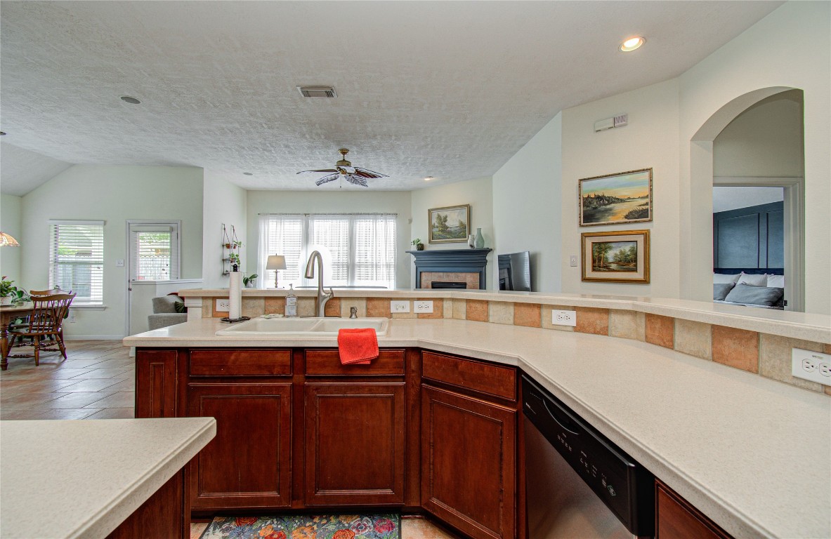 20007 Alcea Court Spring, TX 77379 - Photo 22 of 43 This photo showcases a spacious, open-concept kitchen with a large island featuring dark wood cabinetry and light countertops. The kitchen overlooks a cozy living area with a fireplace and large windows, providing ample natural light. Adjacent to the kitchen is a dining space with tiled flooring, creating a seamless flow between areas.