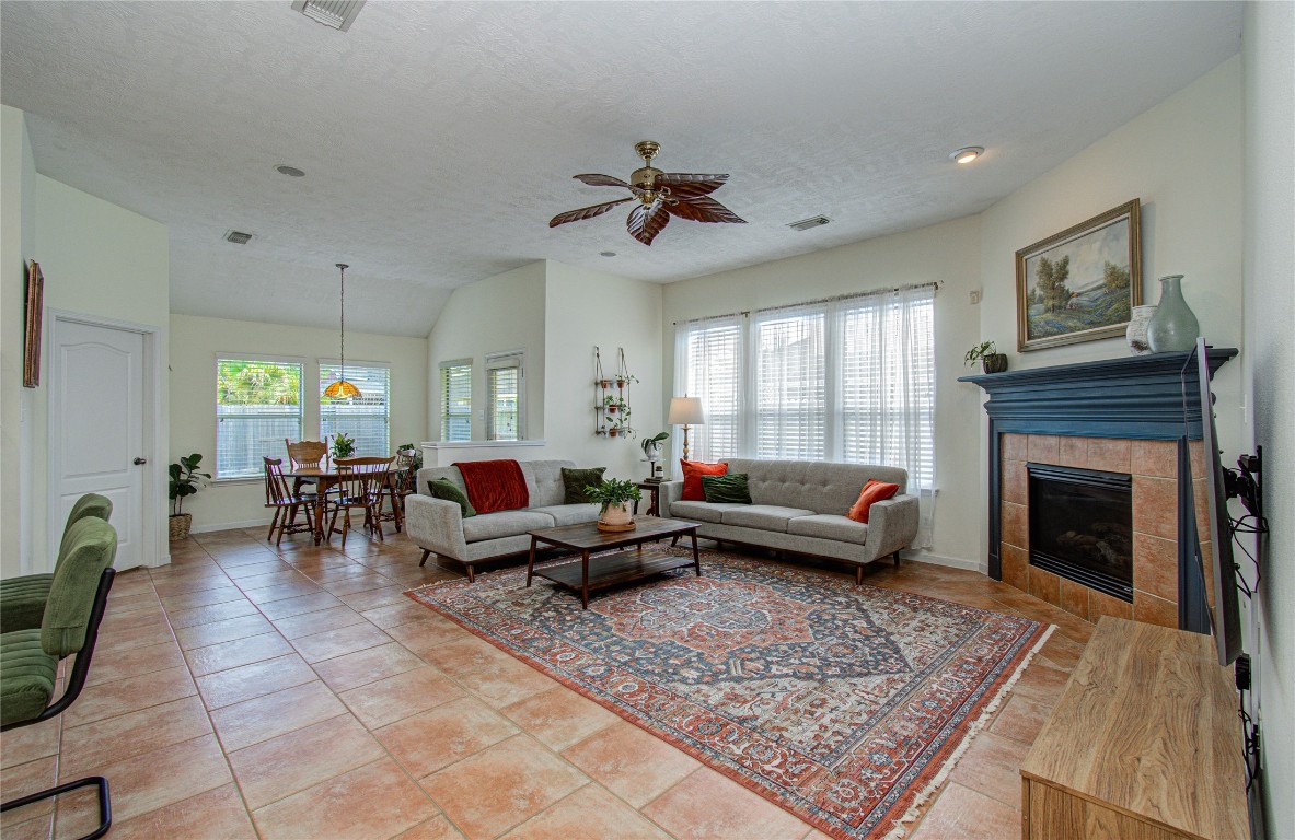 20007 Alcea Court Spring, TX 77379 - Photo 24 of 43 This inviting living area features an open concept design with a cozy fireplace, large windows for natural light, and a ceiling fan. The space seamlessly connects to a dining area, creating an ideal setting for relaxation and entertaining.
