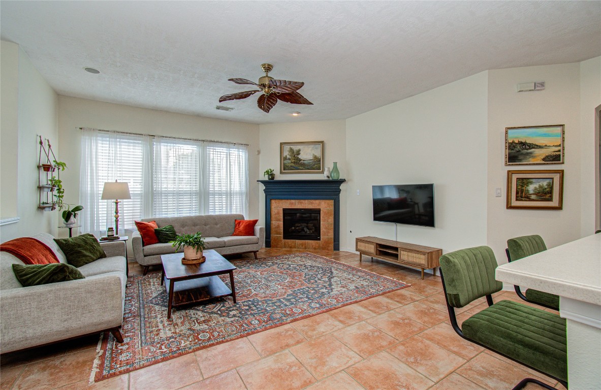 20007 Alcea Court Spring, TX 77379 - Photo 25 of 43 A cozy living room with natural light, featuring a fireplace, modern furnishings, and a wall-mounted TV. The space is accented with a large patterned rug and greenery, creating a warm and inviting atmosphere.