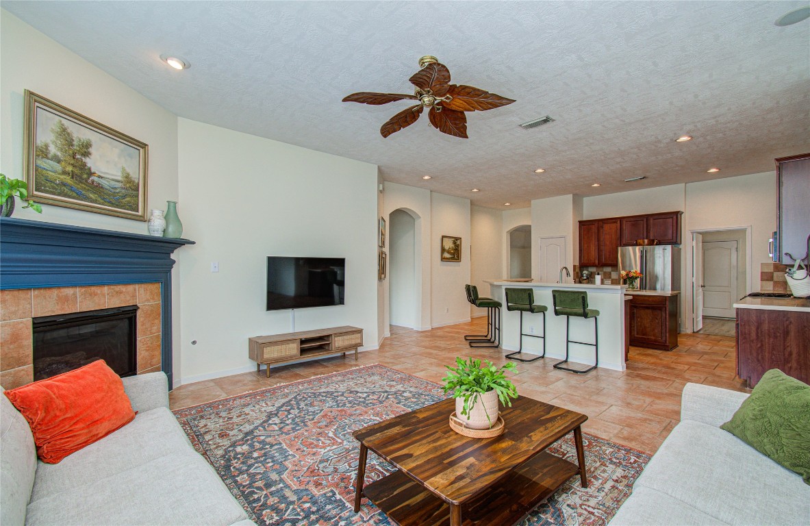20007 Alcea Court Spring, TX 77379 - Photo 43 of 43 This spacious living area features an open floor plan with a cozy fireplace, modern ceiling fan, and stylish tile flooring. The room seamlessly connects to a kitchen with a breakfast bar and stainless steel appliances, offering a perfect setting for entertaining.