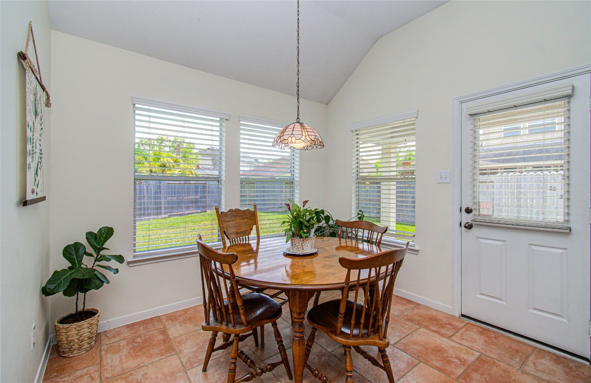 20007 Alcea Court Spring, TX 77379 - Photo 27 of 43 A bright and cozy dining area with a round wooden table and four chairs, featuring large windows with blinds, a hanging light fixture, and a view of the backyard. The space has a potted plant and a door leading outside.
