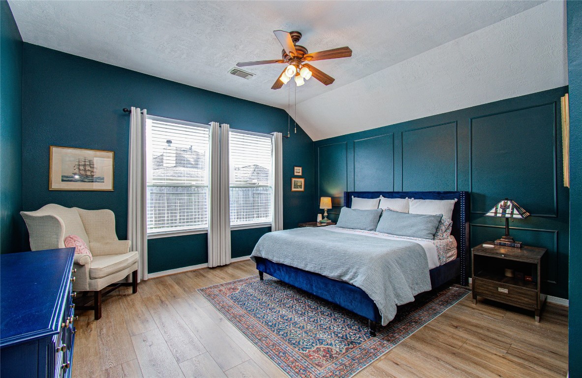 20007 Alcea Court Spring, TX 77379 - Photo 33 of 43 This primary bedroom features a cozy, modern design with deep teal walls and wood flooring. It includes a comfortable bed, a ceiling fan, ample natural light from two windows, and tasteful decor, creating a relaxing atmosphere.