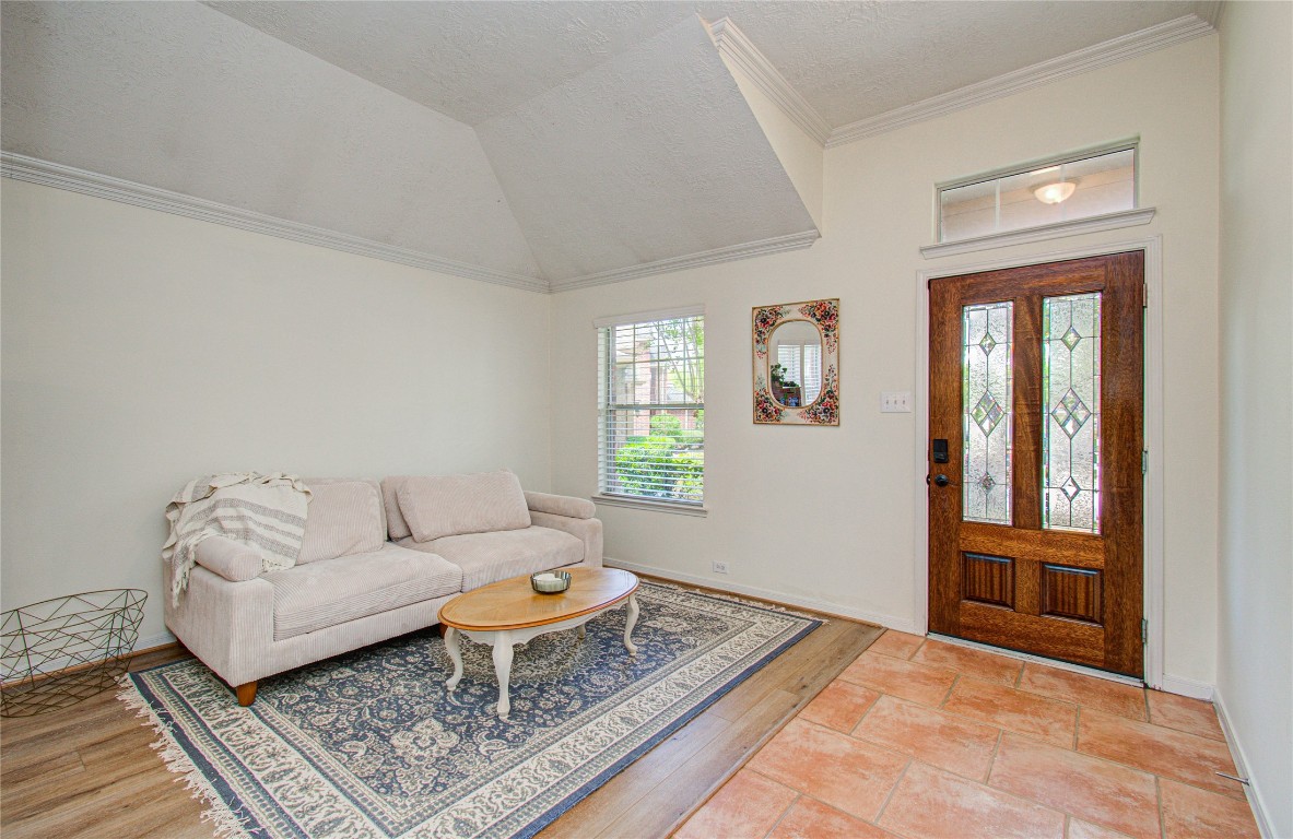 20007 Alcea Court Spring, TX 77379 - Photo 6 of 43 Bright and inviting entryway with high ceilings, featuring a cozy sitting area. The space includes a large window for natural light, a stylish wooden front door with decorative glass panels, and a mix of tile and wood flooring.