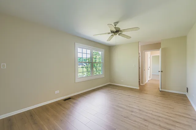 an empty room with wooden floor ceiling fan and windows