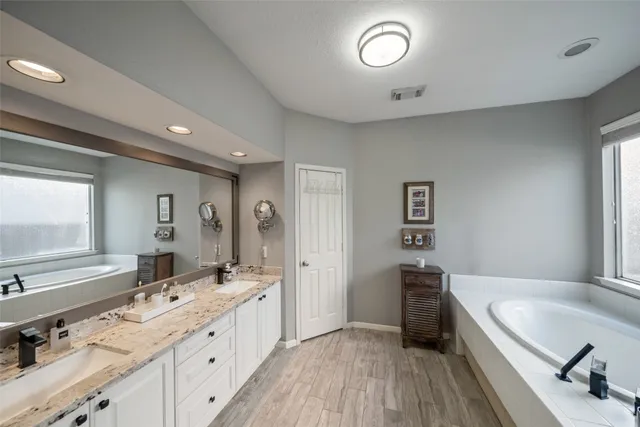 a spacious bathroom with a granite countertop double vanity sink a mirror and a bathtub