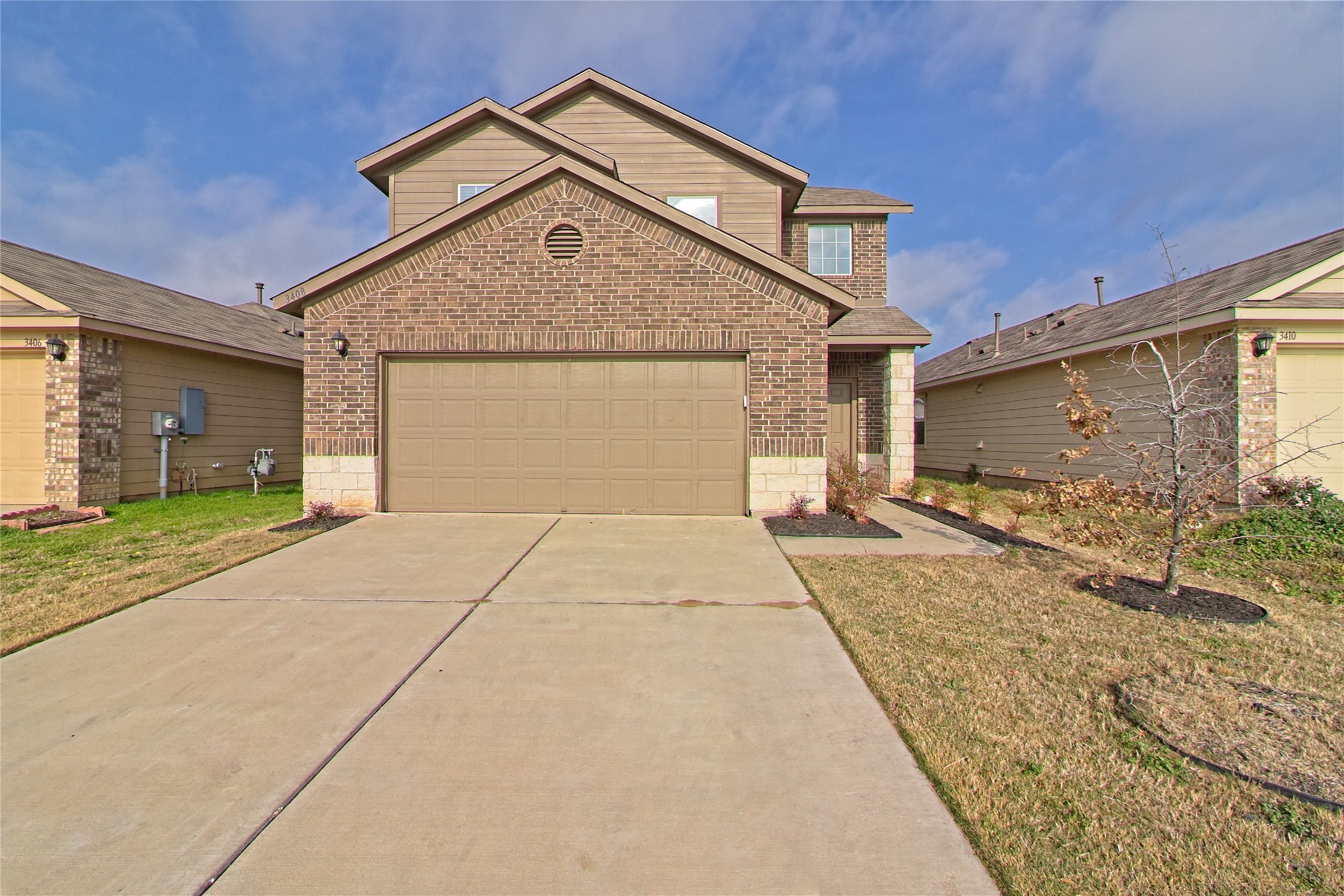Traditional home featuring brick siding, driveway, a garage, and a front lawn
