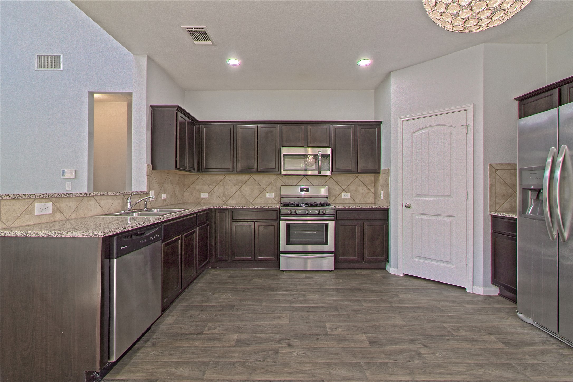 3408 Tilmon Ln. Austin, TX 78725 - Photo 13 of 35 Kitchen featuring stainless steel appliances, dark wood finish cabinets, light stone countertops, dark wood-type flooring, and backsplash