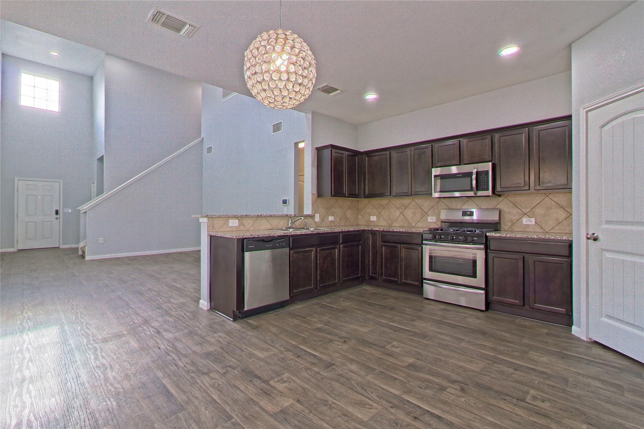 3408 Tilmon Ln. Austin, TX 78725 - Photo 14 of 35 Kitchen featuring dark wood finish cabinetry, stainless steel appliances, dark wood-style flooring, suspended lighting, and decorative backsplash