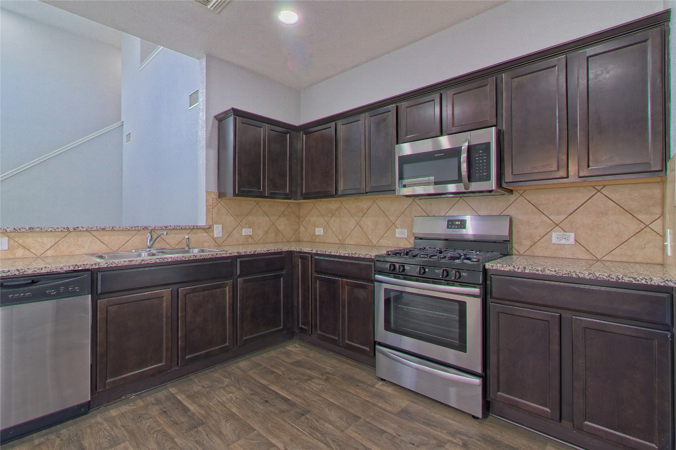3408 Tilmon Ln. Austin, TX 78725 - Photo 16 of 35 Kitchen with dark wood finish cabinets, stainless steel appliances, light stone countertops, dark wood finished floors, and tasteful backsplash