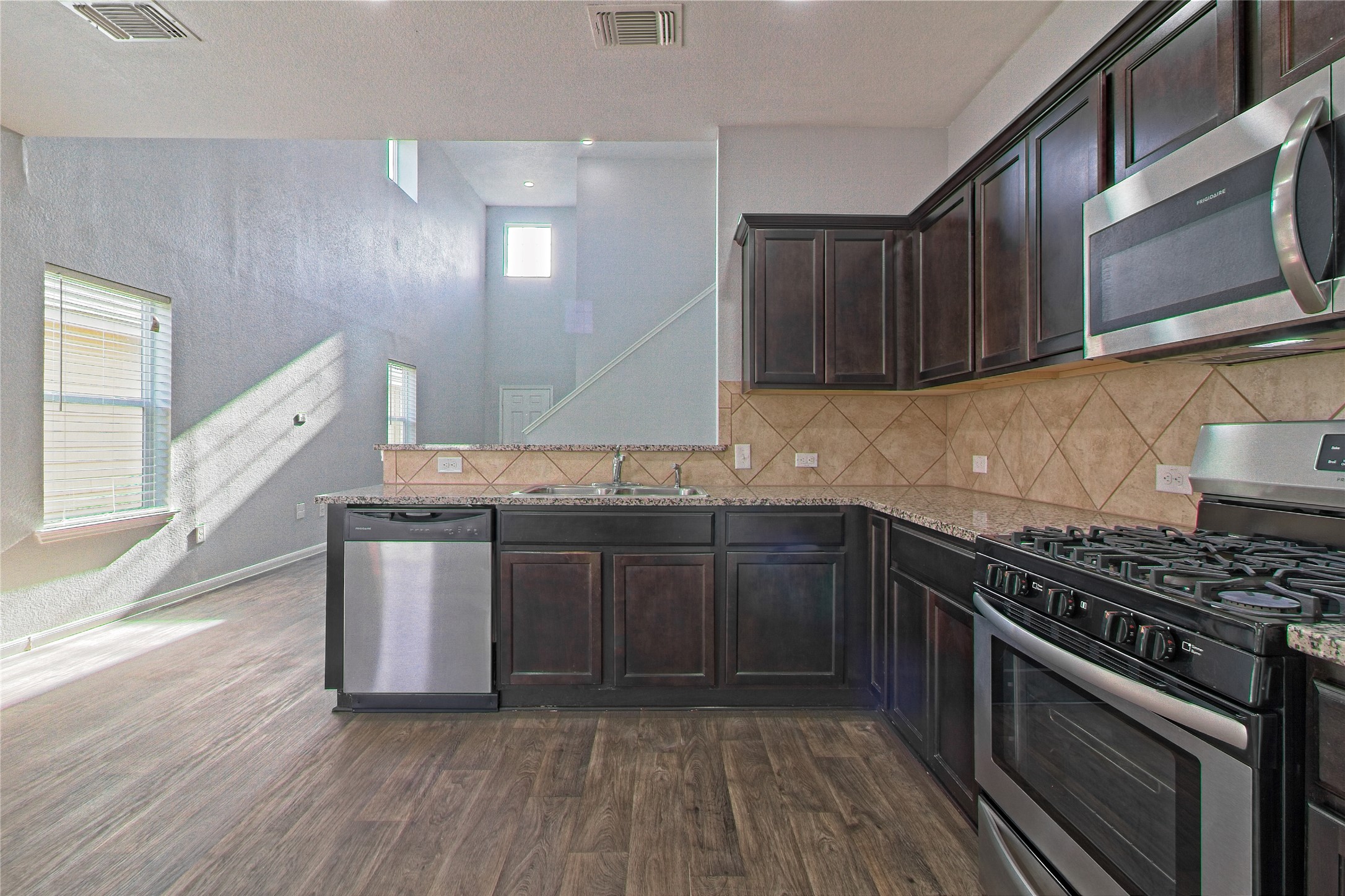 3408 Tilmon Ln. Austin, TX 78725 - Photo 17 of 35 Kitchen with stainless steel appliances, dark wood finish cabinets, dark wood-style flooring, light stone counters, and tasteful backsplash