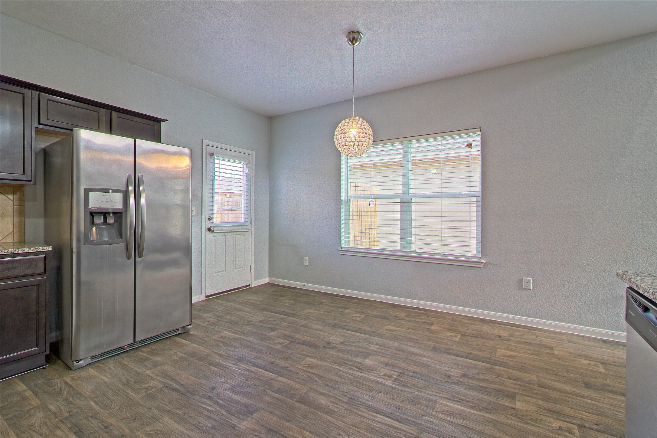 3408 Tilmon Ln. Austin, TX 78725 - Photo 18 of 35 Kitchen featuring dark wood finish cabinets, stainless steel appliances, a textured wall, dark wood-type flooring, and light stone counters