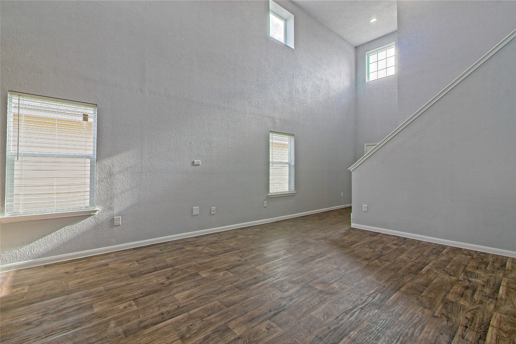 3408 Tilmon Ln. Austin, TX 78725 - Photo 9 of 35 Unfurnished living room featuring a high ceiling, healthy amount of natural light, dark wood-style floors, and a textured wall
