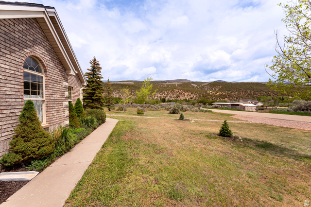 7343 North Sawtooth Cv Road Vernal, UT 84078 - Photo 56 of 64 Brick exterior with arched window, concrete walkway, mature evergreen landscaping, and expansive yard with distant mountain backdrop
