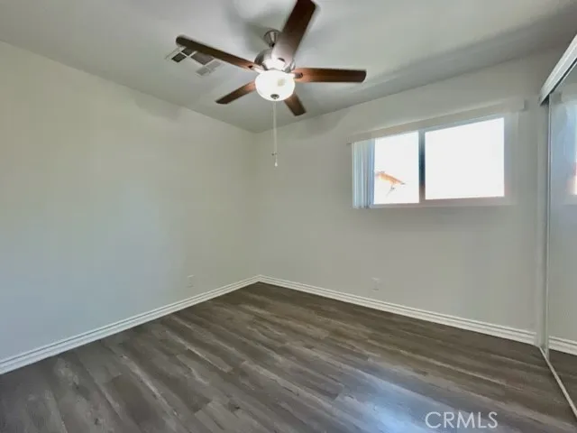 an empty room with wooden floor fan and windows