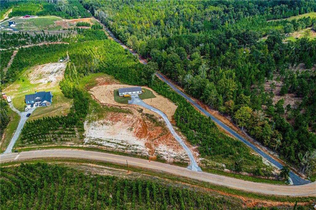 Aerial view showcasing a sprawling property featuring mature forest surroundings, cleared land parcels with gravel access roads, a residential structure positioned on the grounds, and a natural water feature winding through the landscape