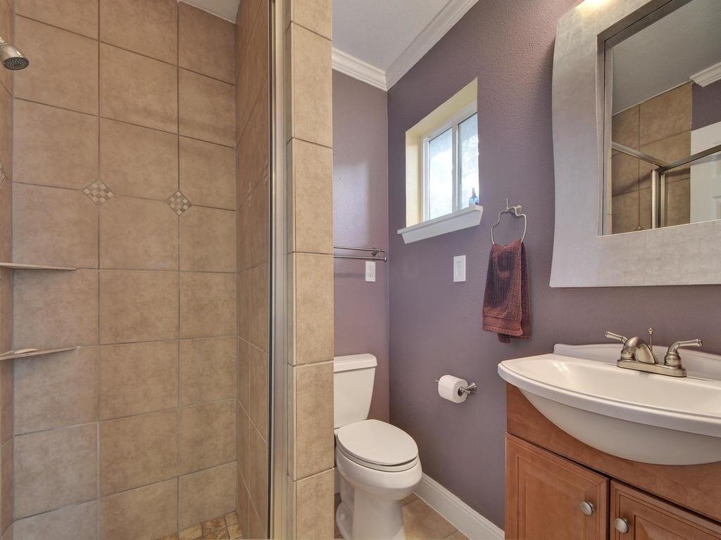 610 West N Loop Boulevard Austin, TX 78751 - Photo 19 of 29 Bathroom featuring a tiled shower with a glass enclosure, a vanity with a white sink, and a mirror with an illuminated frame