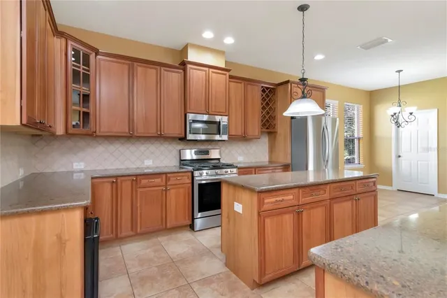 a kitchen with stainless steel appliances granite countertop wooden cabinets a sink a stove a kitchen island and chairs