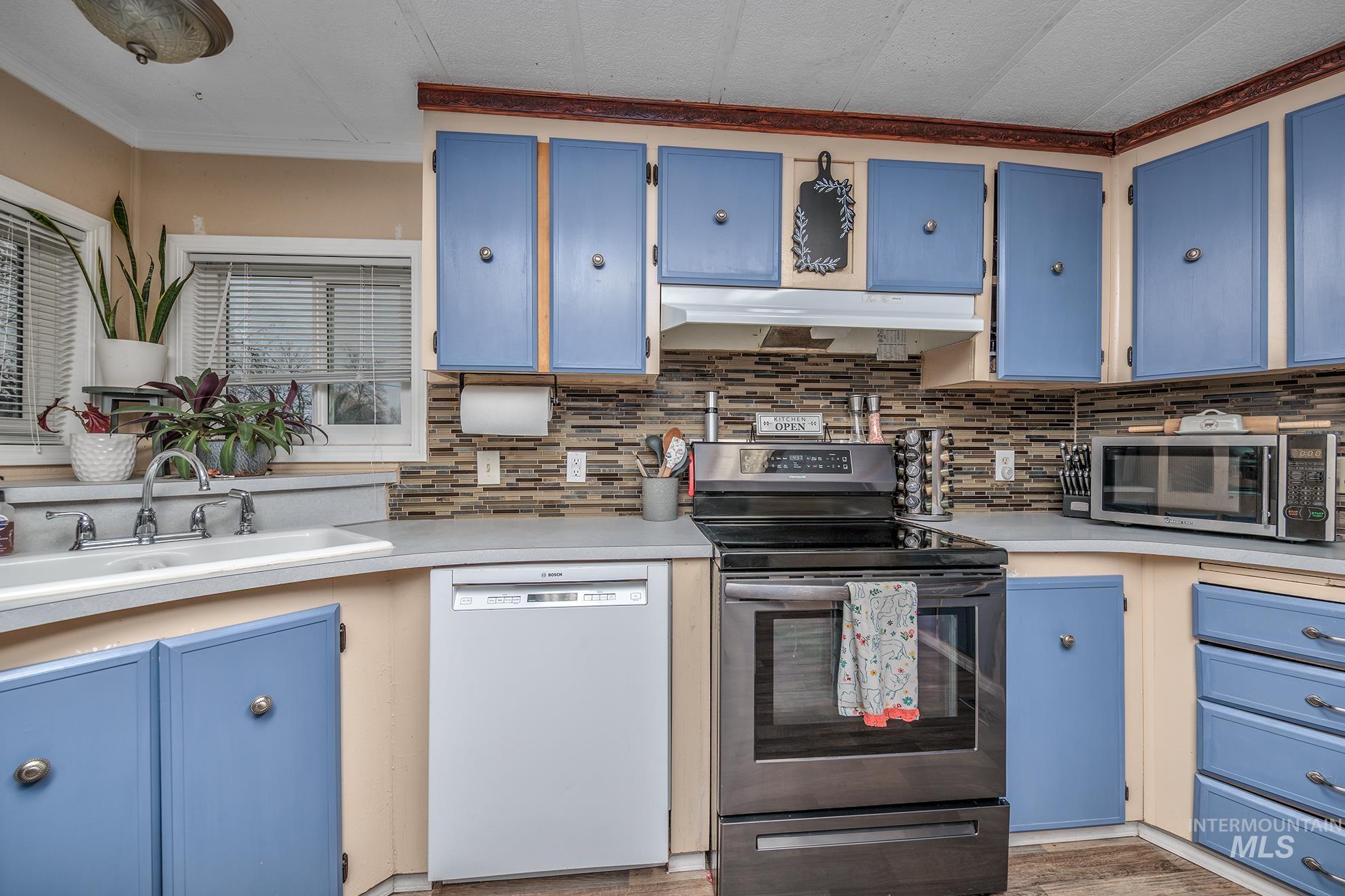 1165 Pioneer Road Weiser, ID 83672 - Photo 16 of 24 Kitchen featuring blue cabinets, stainless steel appliances, light countertops, under cabinet range hood, and crown molding